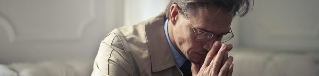 man sitting on couch heads down coping with suicide bereavement