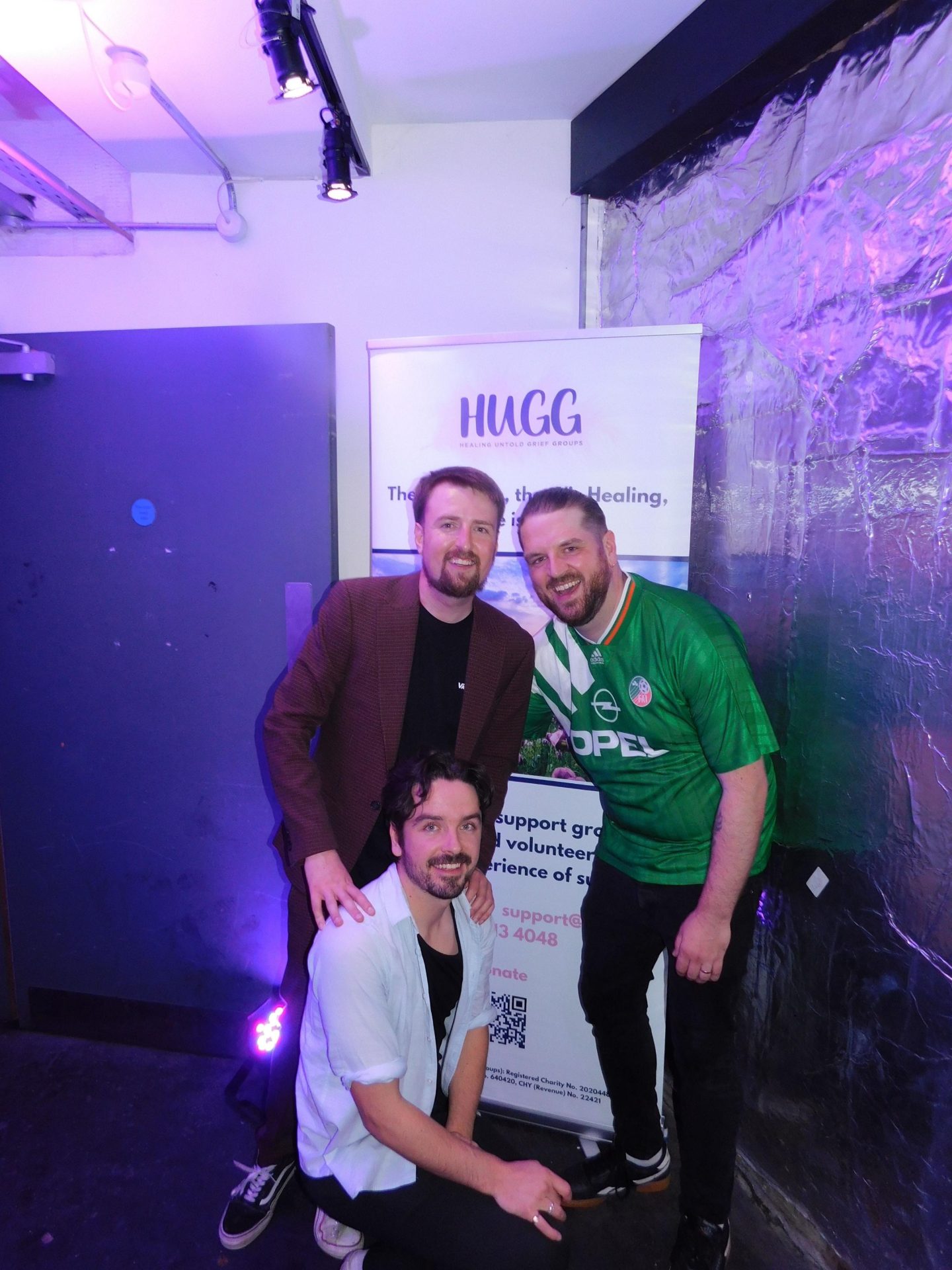 fundraiser craig with his mates in front of a hugg poster at this charity gig