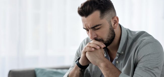 man sitting on couch represent the shame and stigma of suicide loss